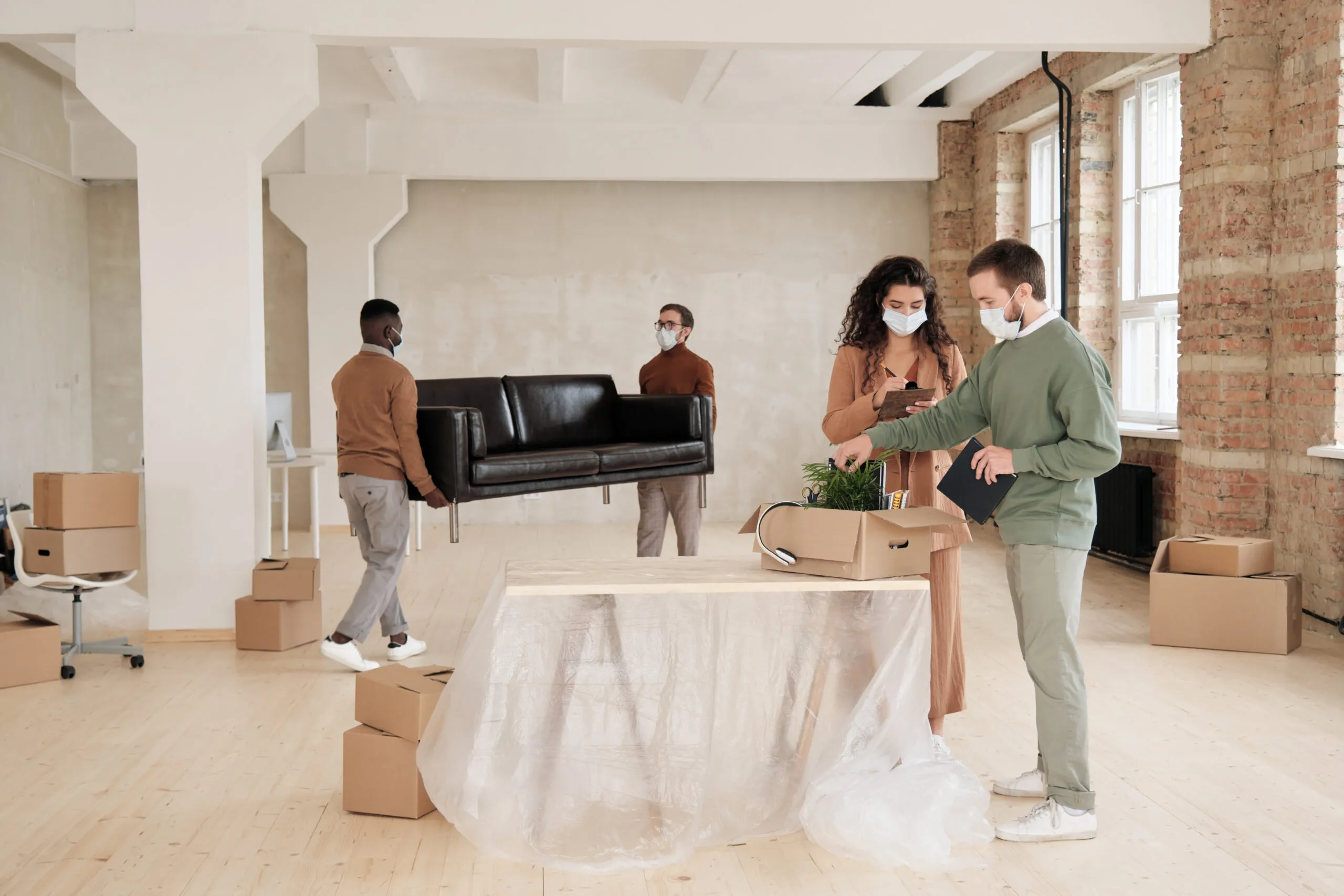 Two professional movers loading cardboard boxes into a moving truck while a young couple watches the relocation process outside their home.