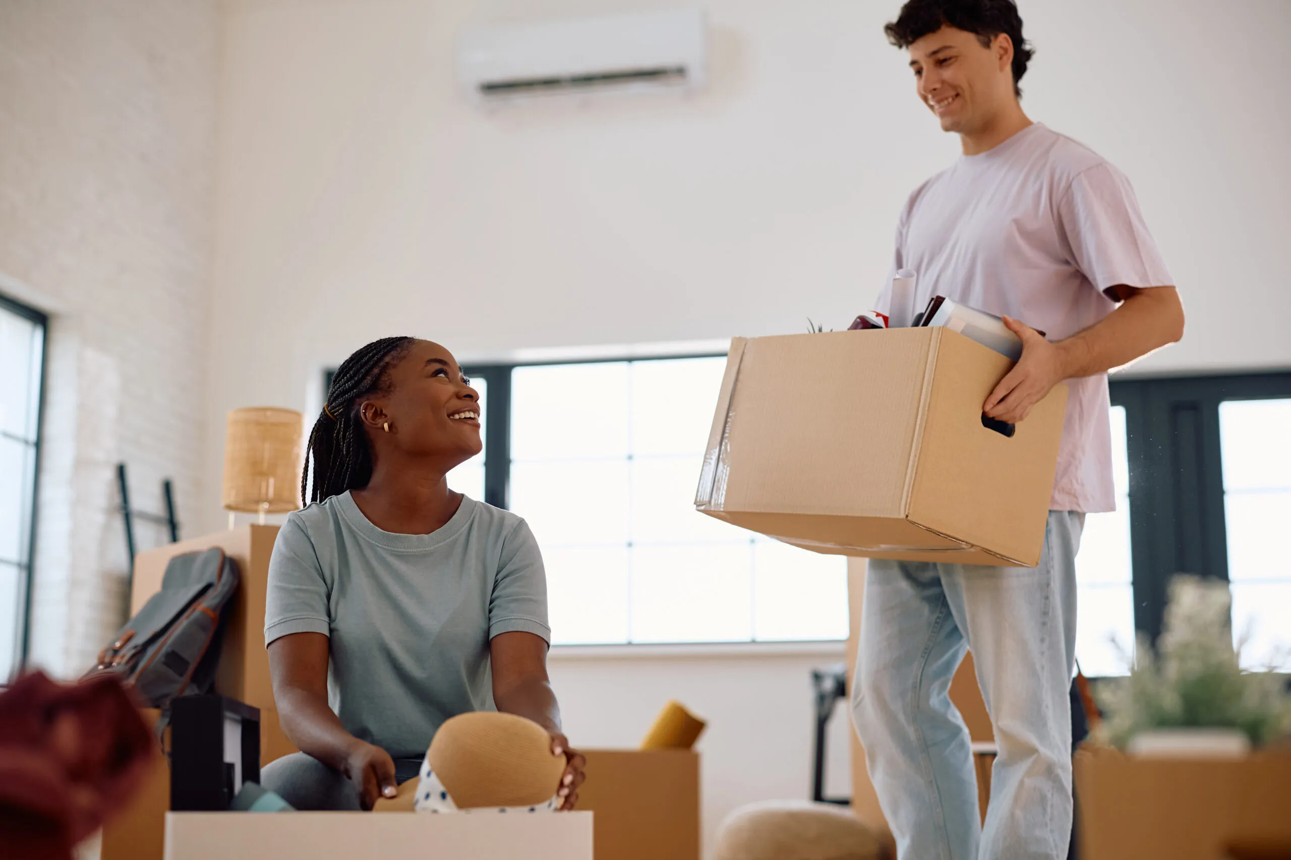 Two professional movers loading cardboard boxes into a moving truck while a couple watches outside their home.